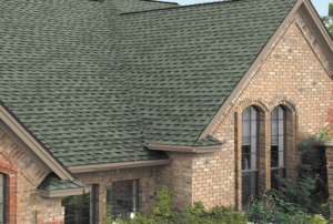 A close-up shot of a brick home with a green-tinged shingle roofing system