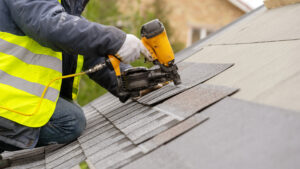 A worker drilling shingles onto a roof